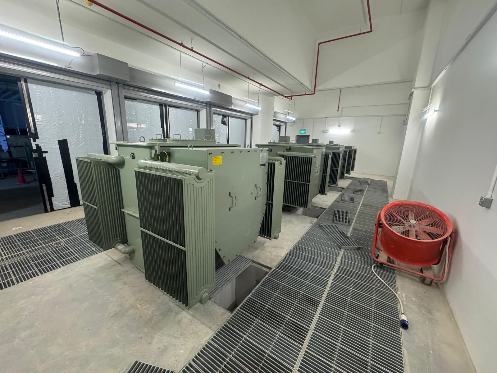 Row of green industrial transformers with metal floor grates.